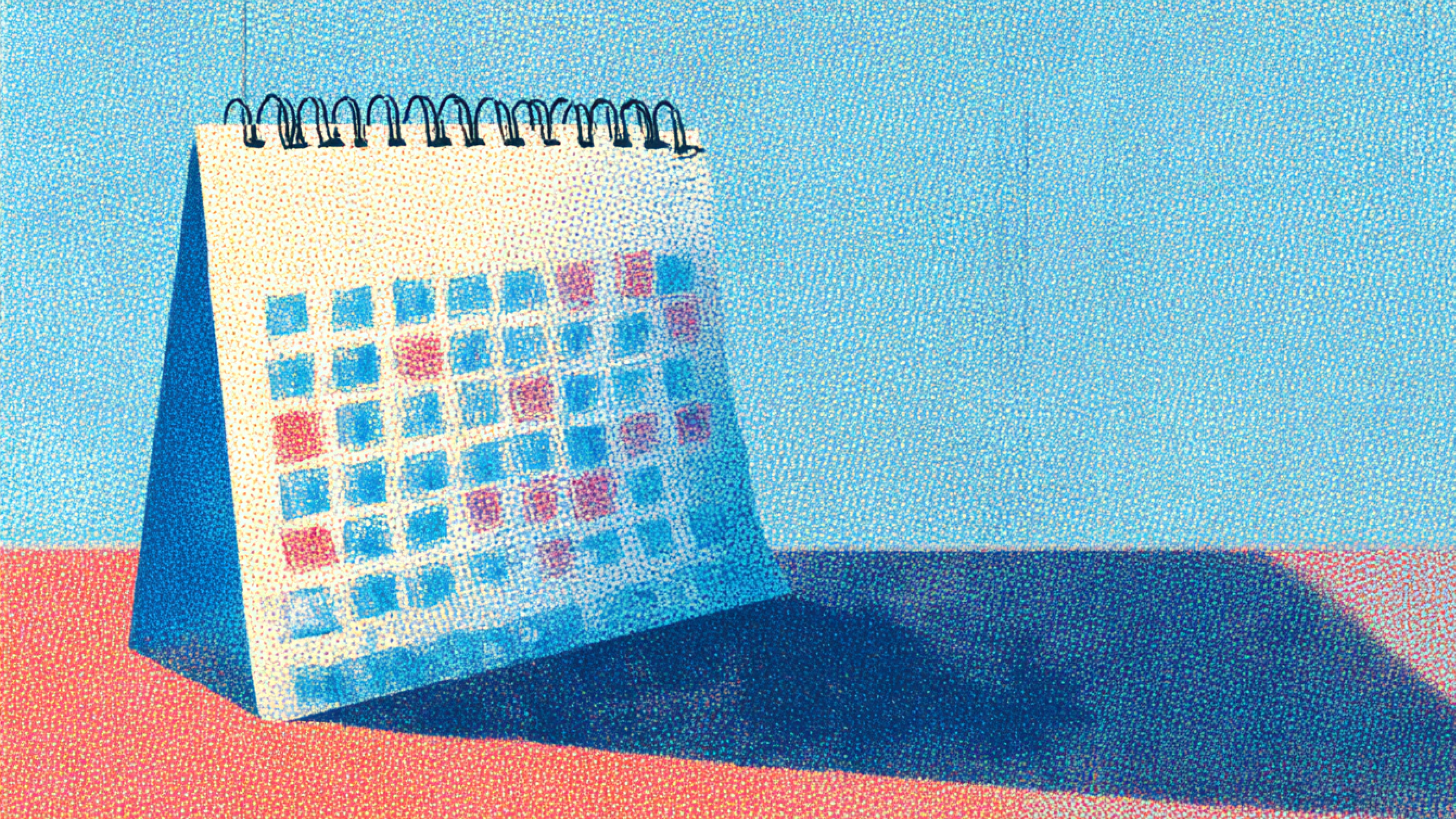 A spiral-bound desk calendar with blue and red marked dates sits on a colorful surface against a blue background.